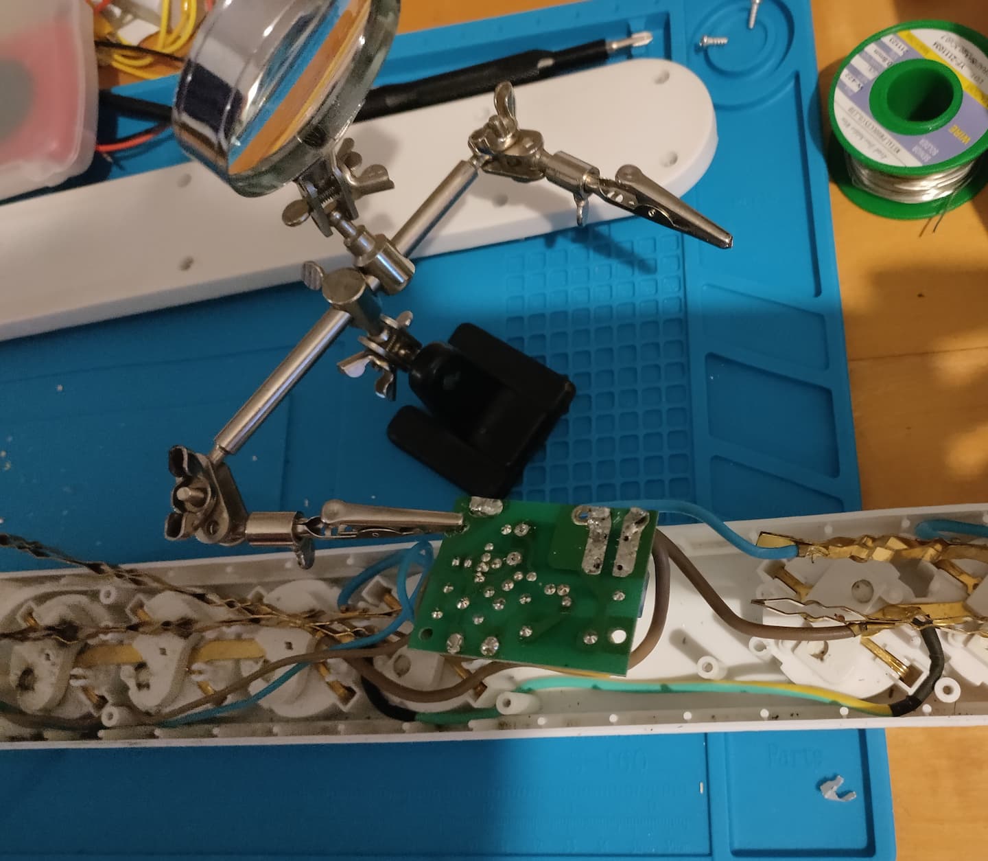 Das Bild zeigt eine Dritte-Hand, in welcher die Steuerplatine der Steckdosenleiste gespannt ist. Im Hintergrund sieht man die geöffnete Leiste