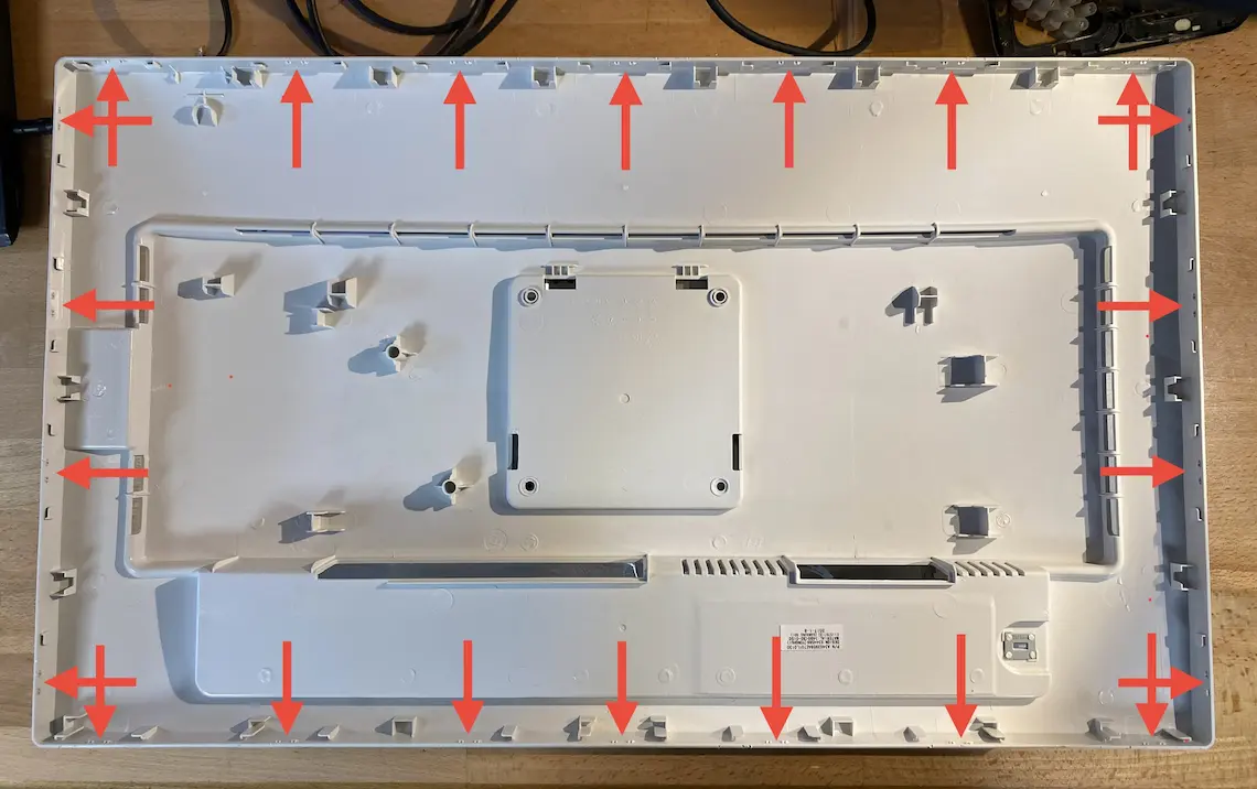 Das Bild zeigt die Rückseite des Monitorgehäuses. Rote Pfeile markieren die Kunststoffclips