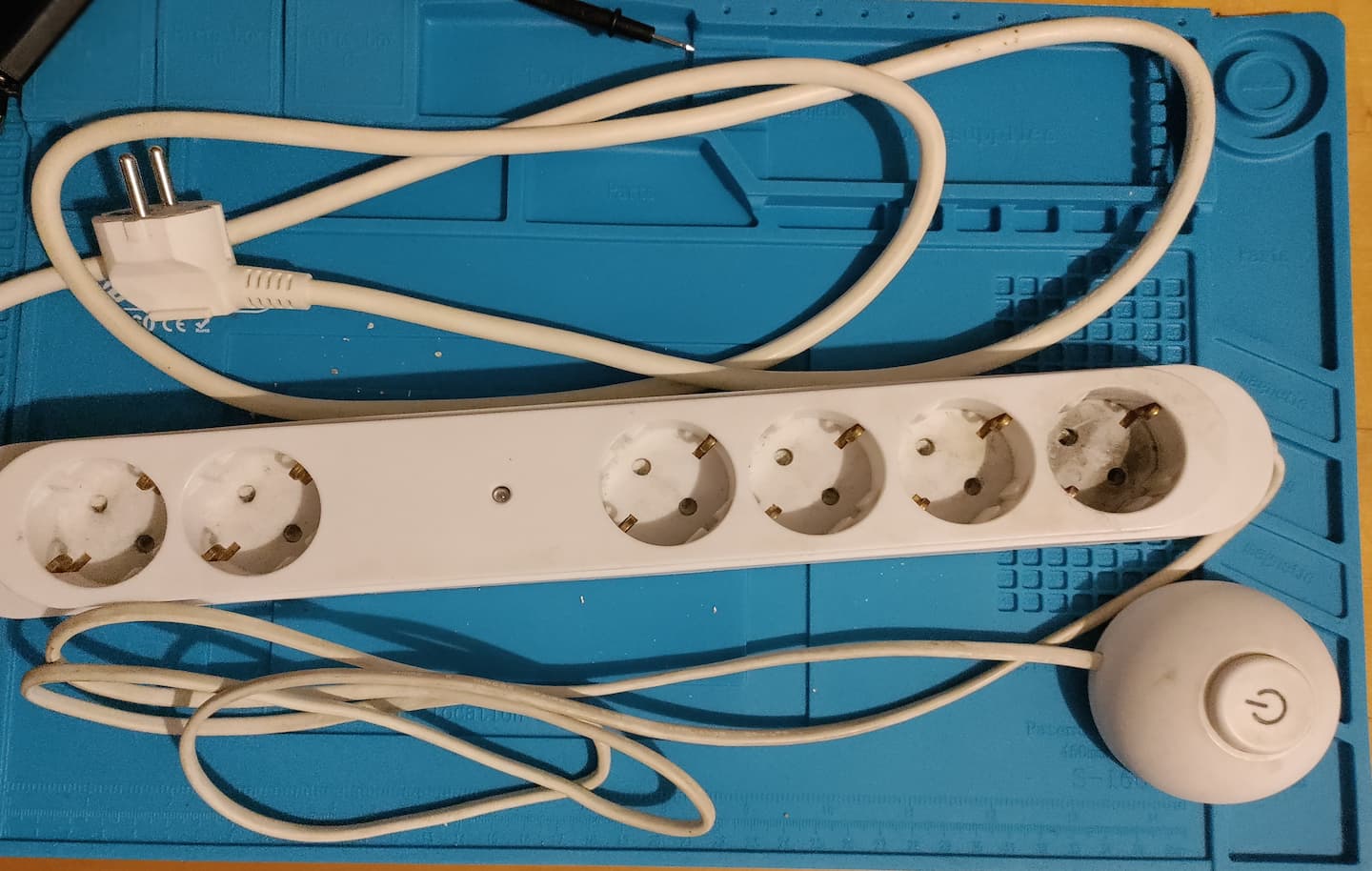 Das Bild zeigt eine Steckdosenleiste auf einer Lötunterlage. Die Steckdosenleiste verfügt über ein Fußpedal zum Schalten der angeschlossenen Geräte.